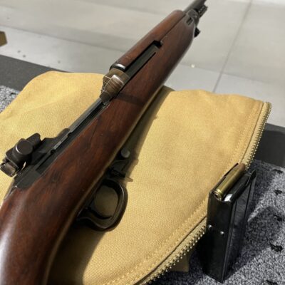 Photo of an M1 Carbine in a shooting lane, resting on its neutral-colored canvas carry case.