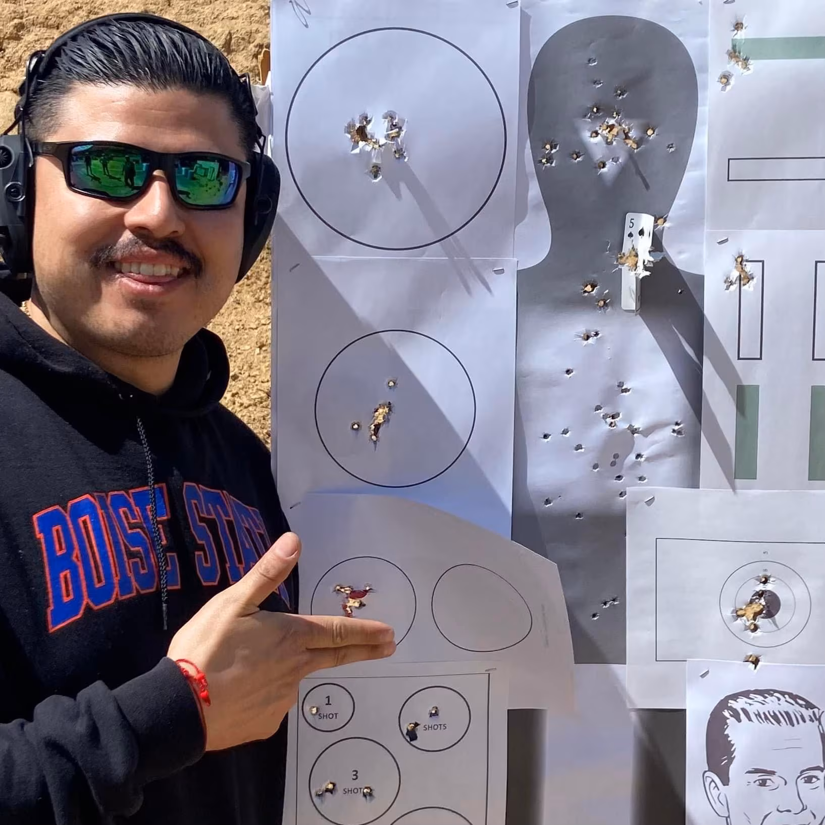 PP Academy (1) A man facing the camera stands next to his Pistol Practice targets, smiling after completing the Pistol Practice class