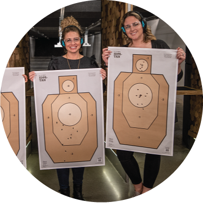 Two women smiling and holding up their shooting targets, looking happy and proud as they face the camera