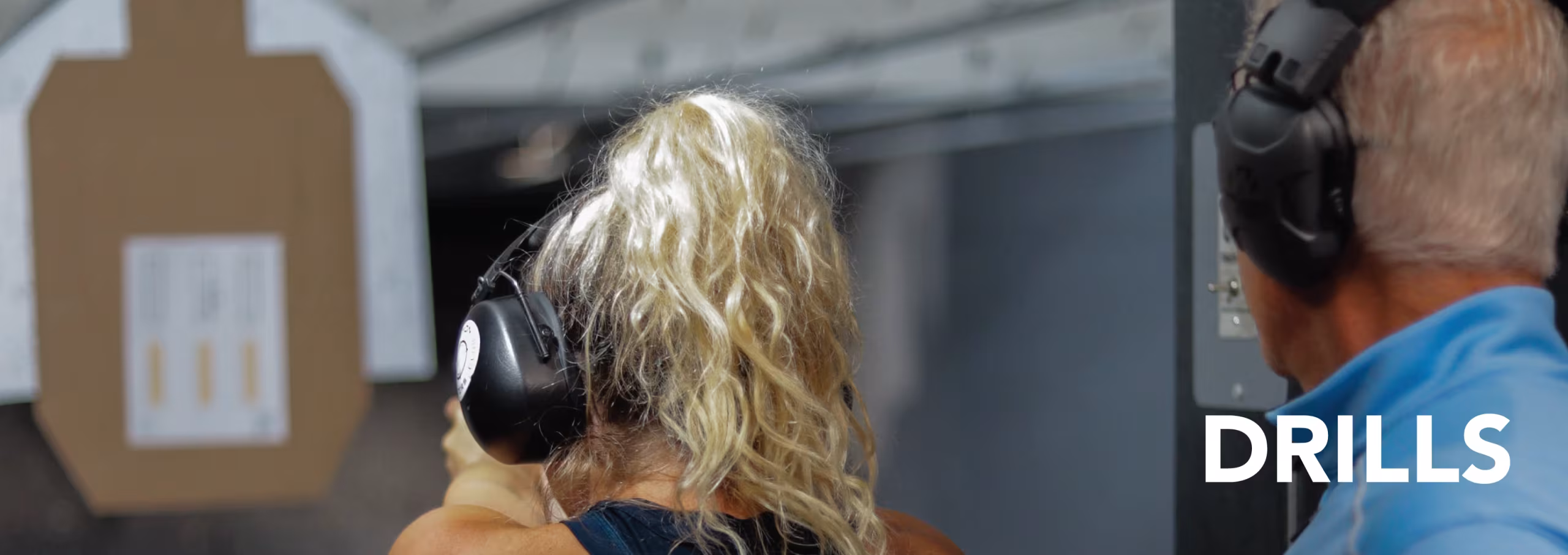 drills-featured A woman shooting at a specialized target under the supervision of an instructor at a shooting range, with the word 'DRILLS' superimposed in the lower right corner